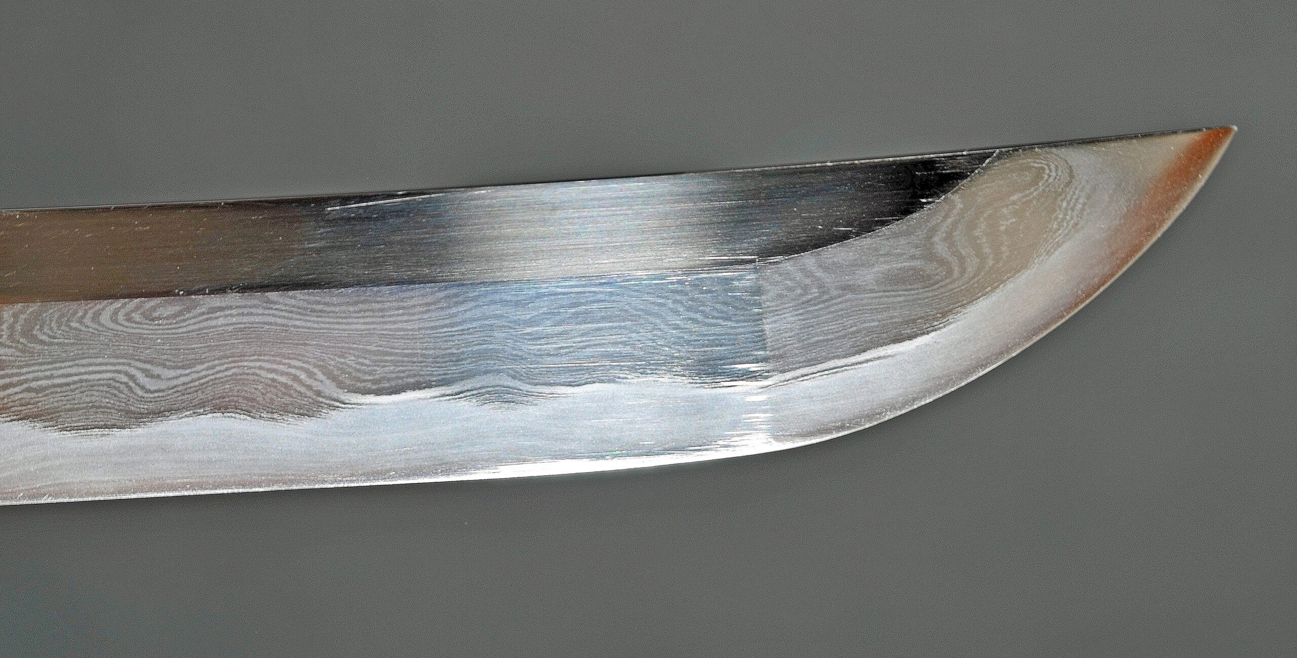 Close-up van een katana-bladpunt met het kissaki-punt, de hamon-temperatuurlijn en het boshi-patroon op een goed onderhouden blad gepolijst Japans zwaard